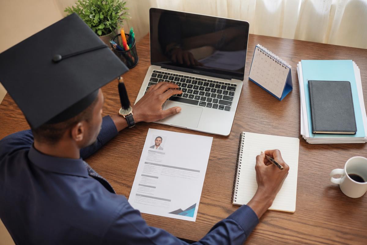 Overhead view of a young Nigerian graduate organizing a job search with a laptop, CV, notebook and calendar