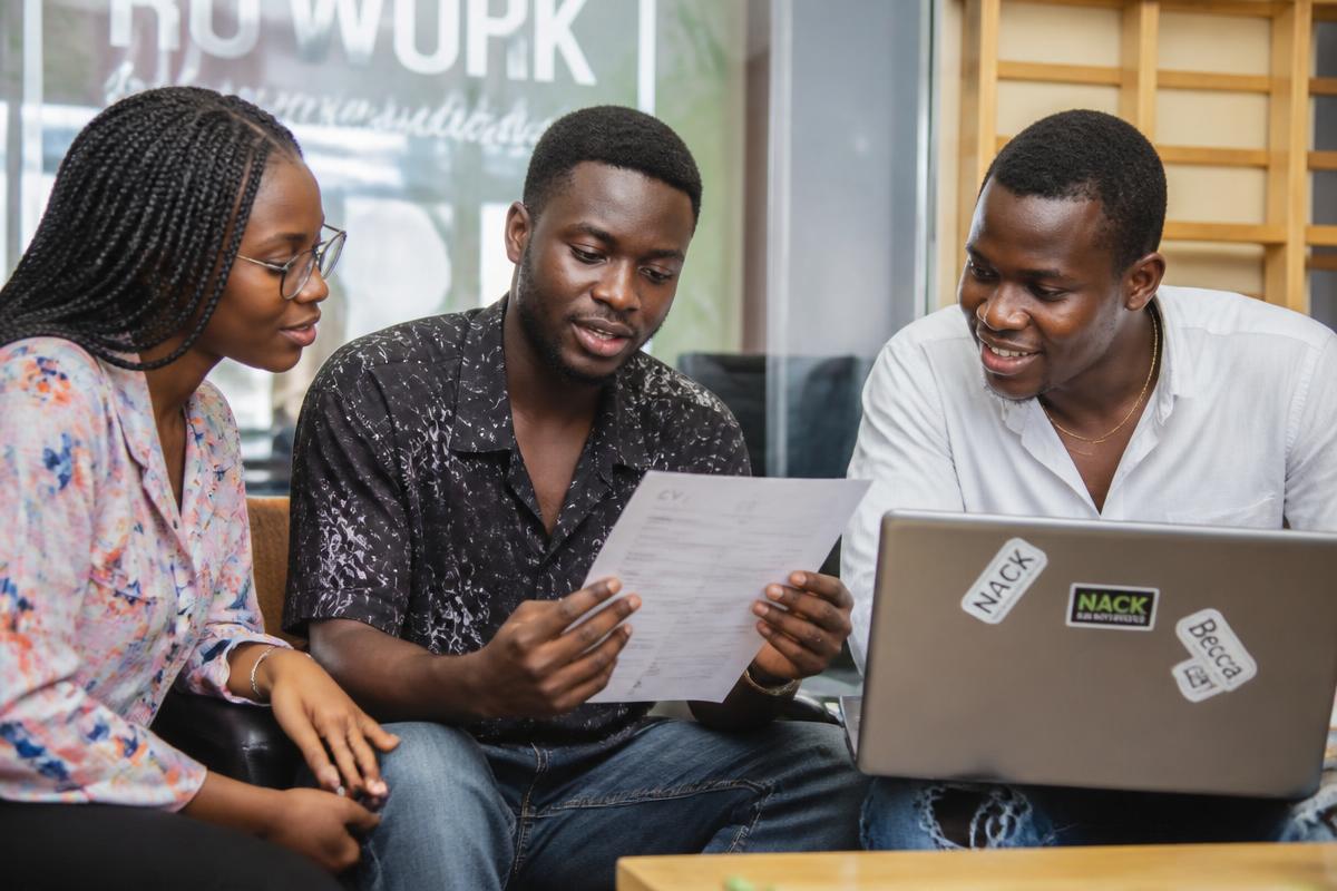 Three young Nigerian adults reviewing a CV and a laptop together in a casual workspace